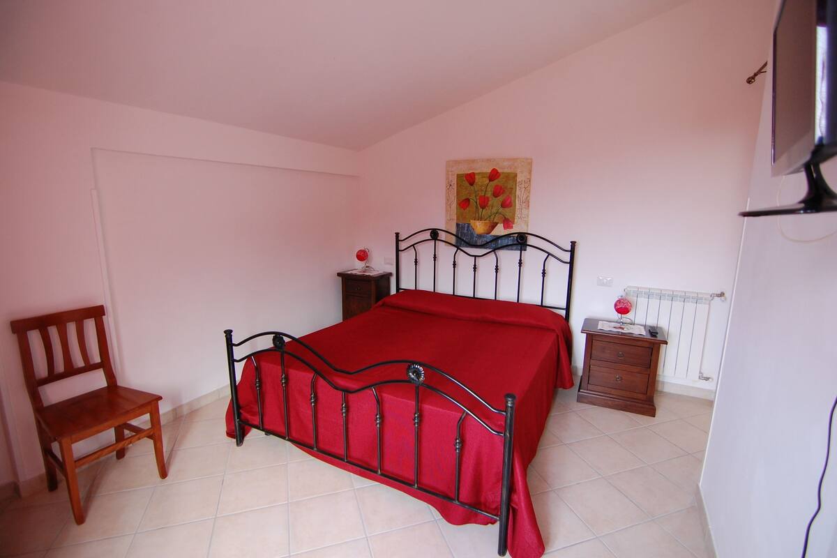 Une chambre à coucher avec un lit, une chaise en bois, une table de chevet et un tableau accroché au mur.