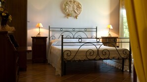 A bedroom with a bed, two bedside tables, a lamp on each table, a wall-mounted decorative plate, and a wooden dresser. - Agriturismo Tempa del Niglio (Ascea)