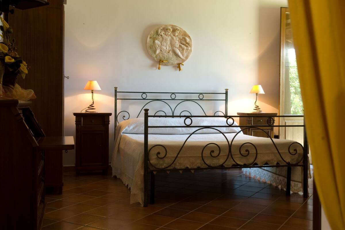 Une chambre à coucher comprenant un lit, deux tables de chevet, une lampe sur chaque table, une assiette décorative accrochée au mur et une commode en bois.