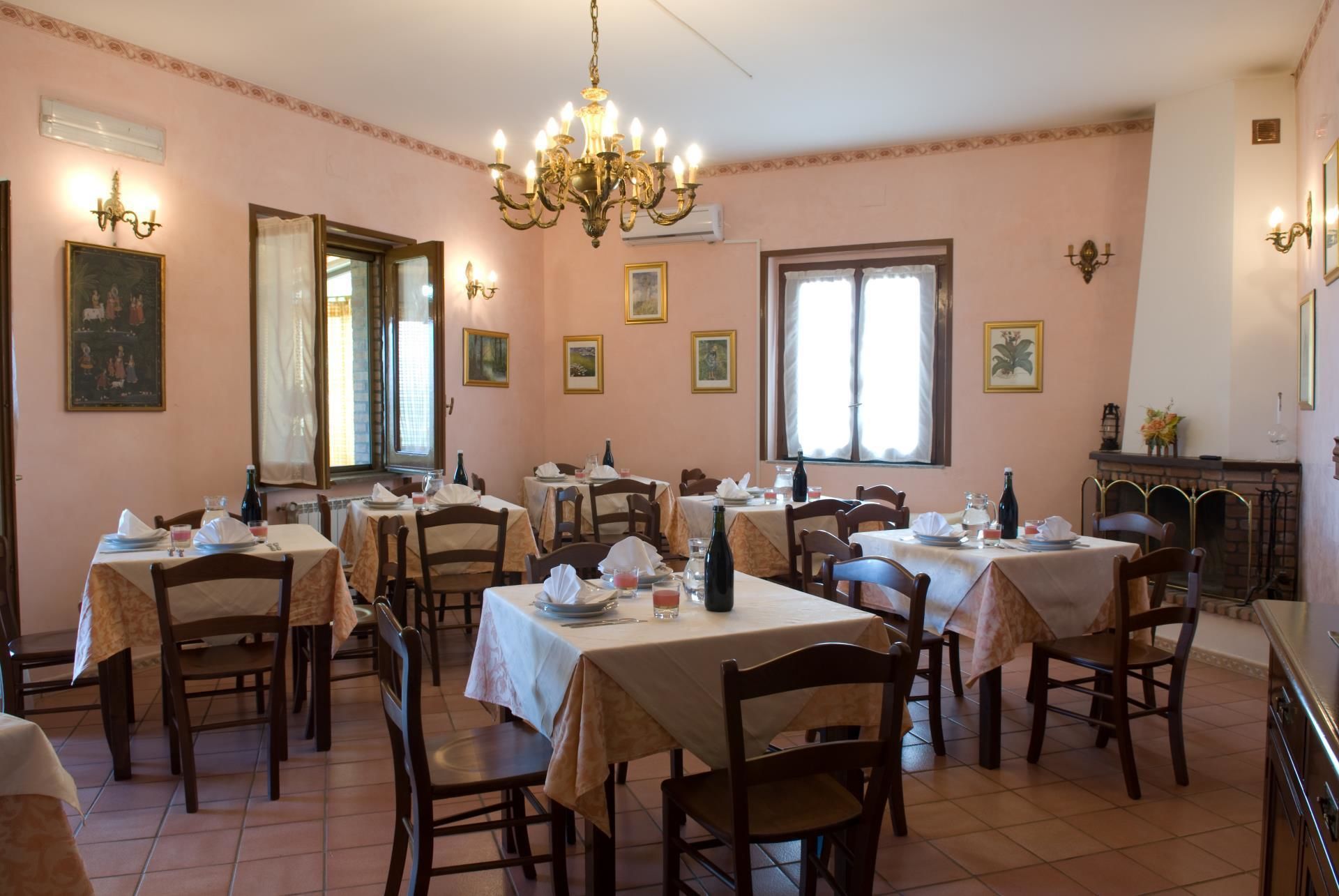 Zona pranzo con diversi tavoli apparecchiati per gli ospiti, un lampadario e opere d'arte incorniciate alle pareti.