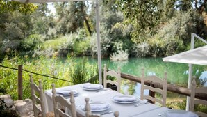 An outdoor dining area with white tables and chairs, set against a backdrop of lush greenery and a body of water. - Posada de Zorita de los Canes (Zorita de los Canes)