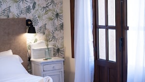 A neatly made bed with white linens, a bedside lamp, a small white nightstand with a vase, and a wooden door with a window. - Posada de Zorita de los Canes (Zorita de los Canes)