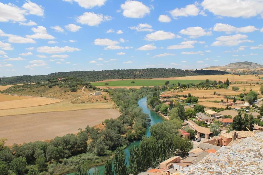 Paisaje rural con un río, campos y edificios dispersos.