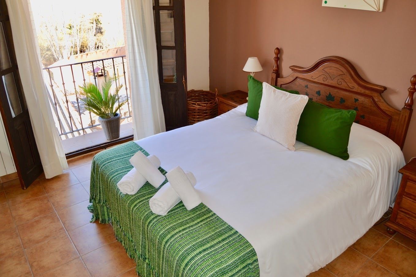 Una cama bien hecha con ropa blanca y verde, un cabecero de madera y una mesita de noche con una lámpara.