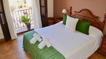 Una cama bien hecha con ropa blanca y verde, un cabecero de madera y una mesita de noche con una lámpara.