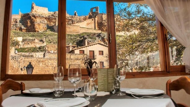 A dining table set with plates, glasses, and cutlery, overlooking a historic stone building with ruins and a view of trees. - Posada de Zorita de los Canes (Zorita de los Canes)
