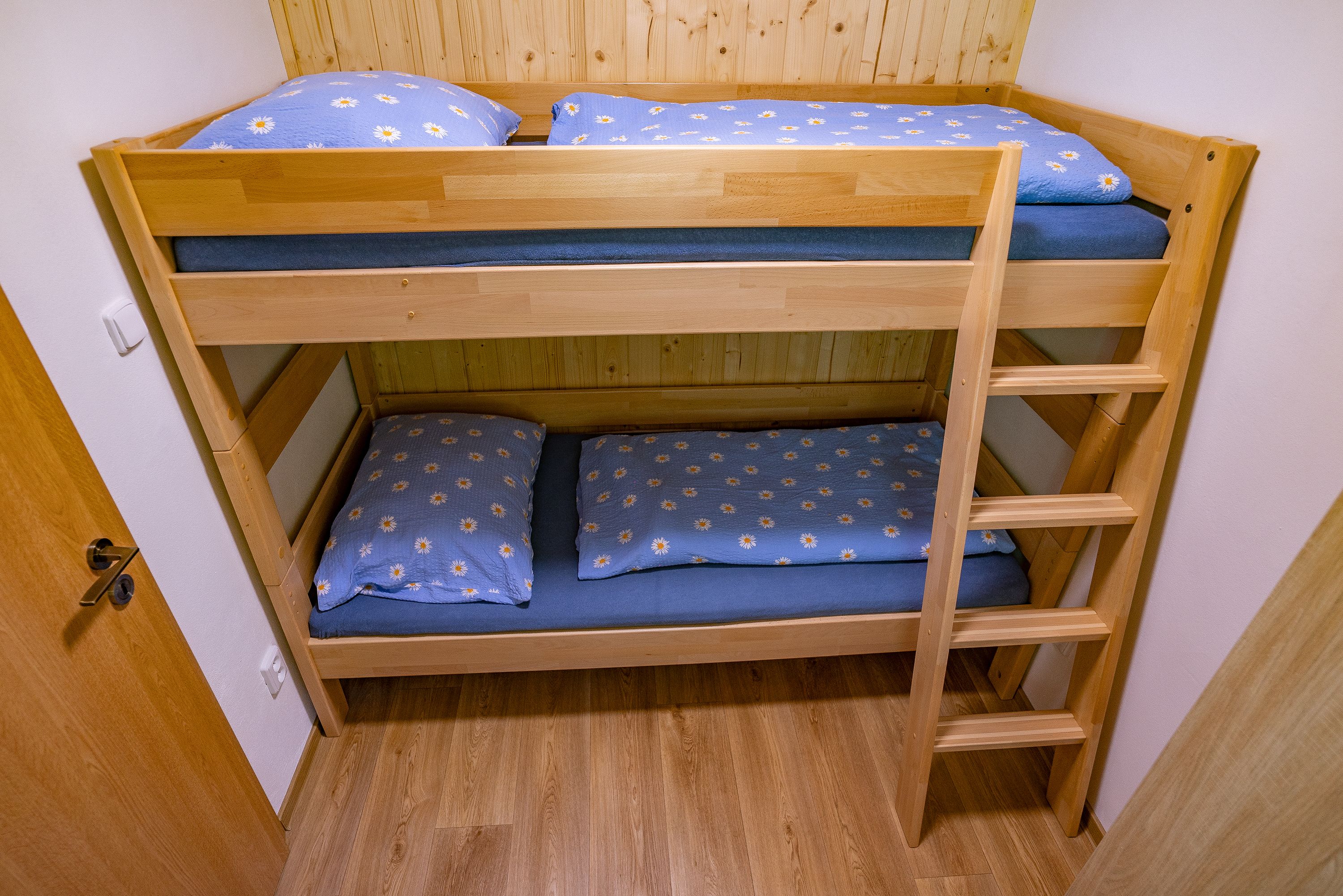 A bunk bed with a wooden frame, blue bedding with a daisy pattern, and a wooden ladder.
