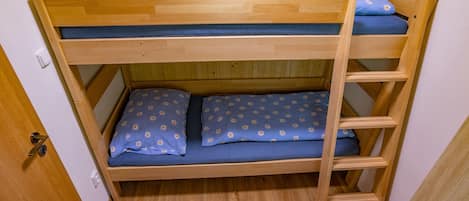 A bunk bed with a wooden frame, blue bedding with a daisy pattern, and a wooden ladder.
