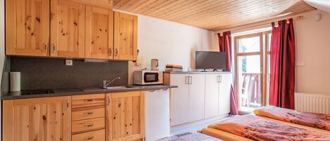 Una habitación compacta con armarios de madera, un microondas, un televisor y una cama con ropa de cama estampada.