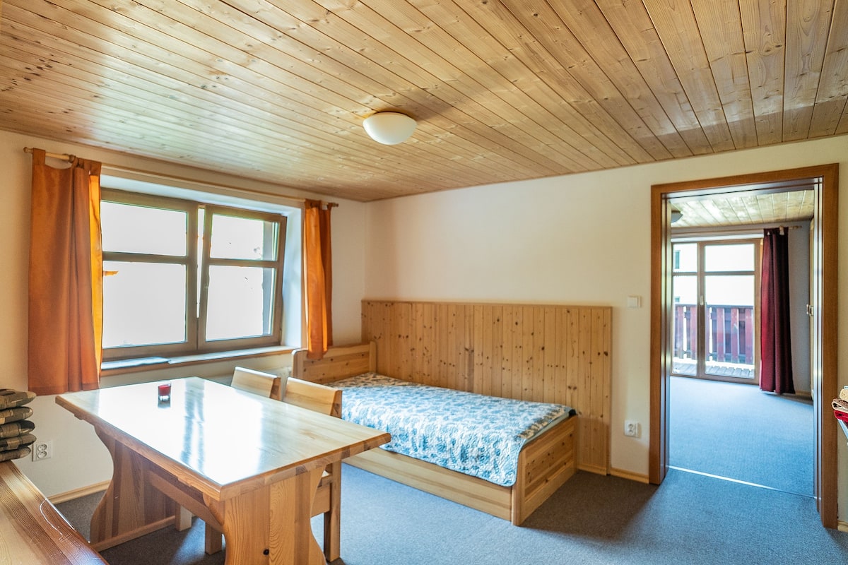 Une pièce avec un plafond en bois, un lit recouvert d’une courtepointe à motifs bleus, une table en bois et une fenêtre avec des rideaux.