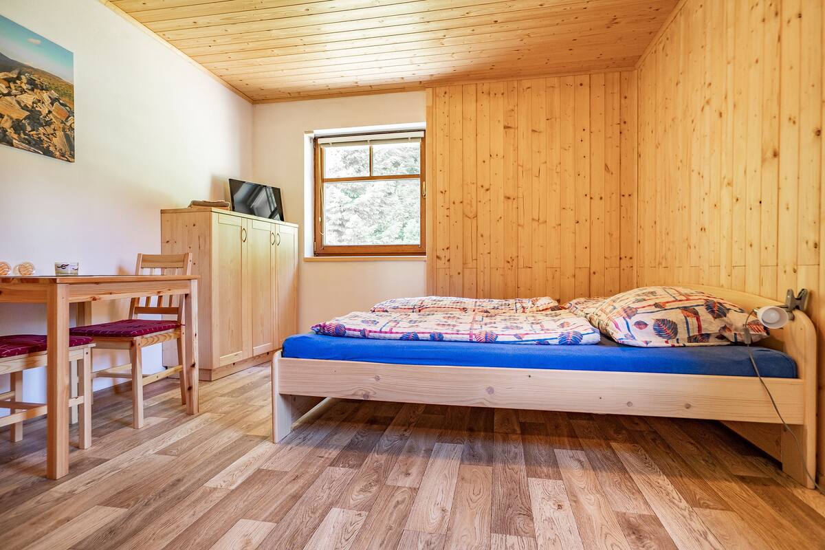 Une petite pièce aux murs lambrissés, comprenant un lit simple, un bureau et une chaise.