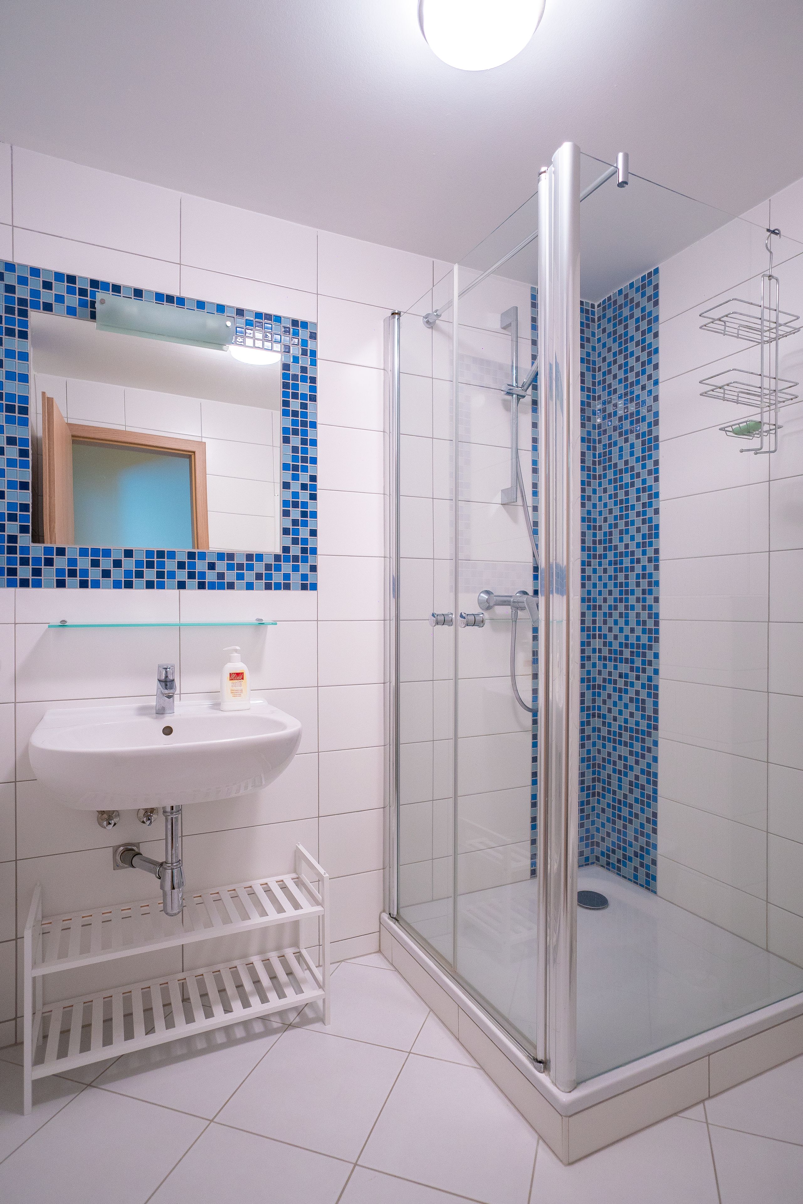 Een badkamer met een glazen douchecabine, een wit wastafelmeubel met zeepdispenser en een spiegel erboven.