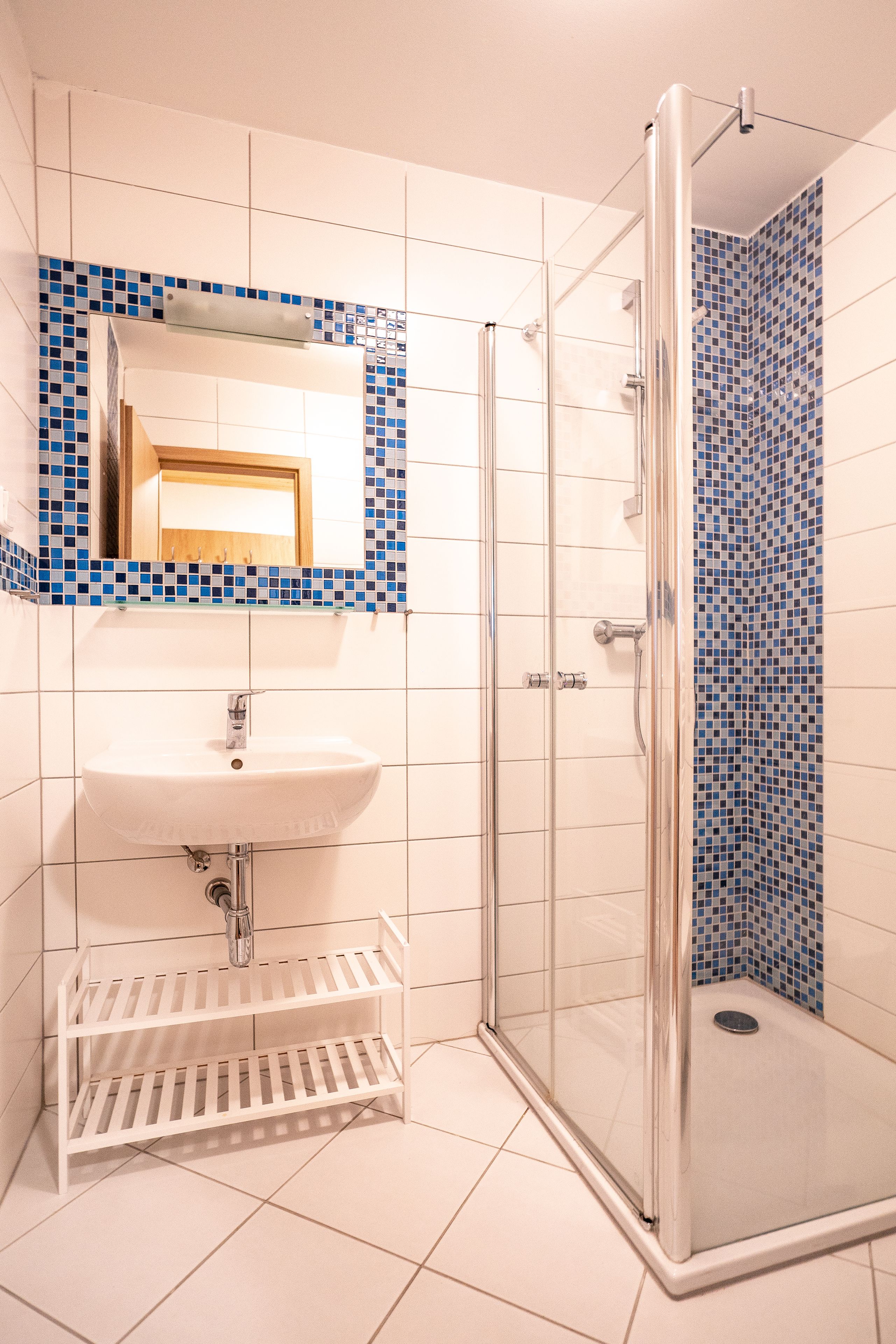 A bathroom with a white sink, a mirror, and a shower with blue mosaic tiles.