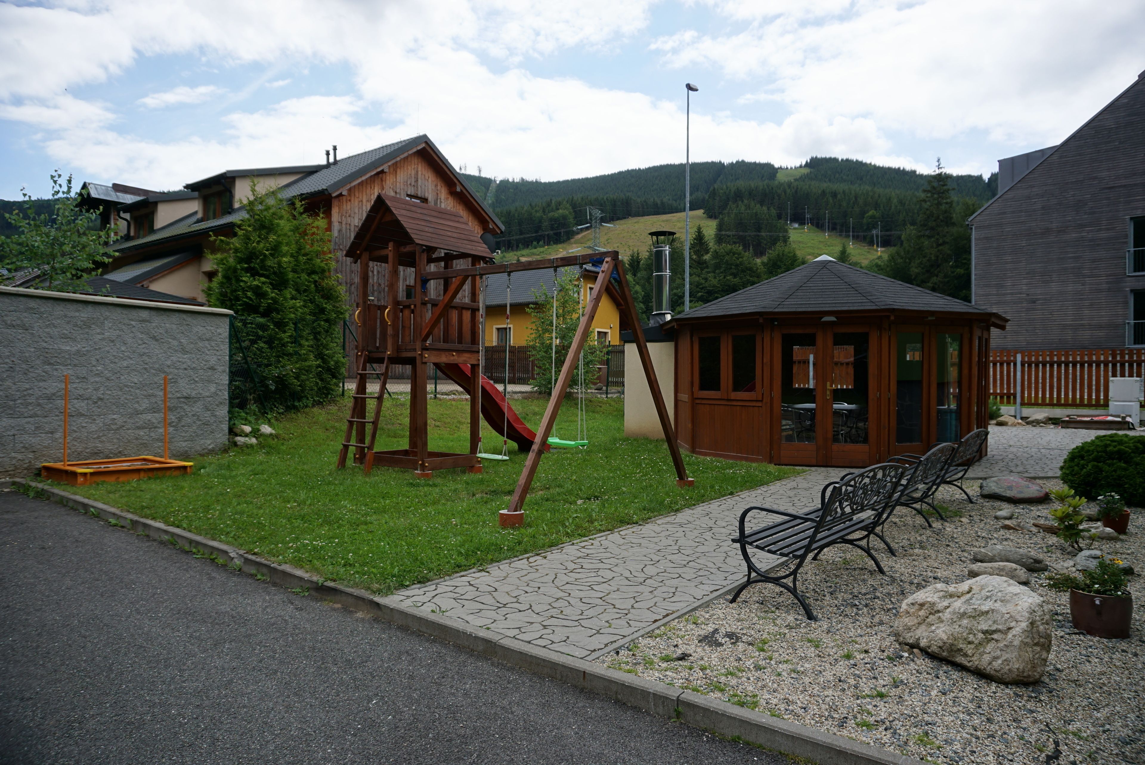 Une aire de jeux avec une balançoire et un toboggan en bois, une petite structure en bois et un banc.