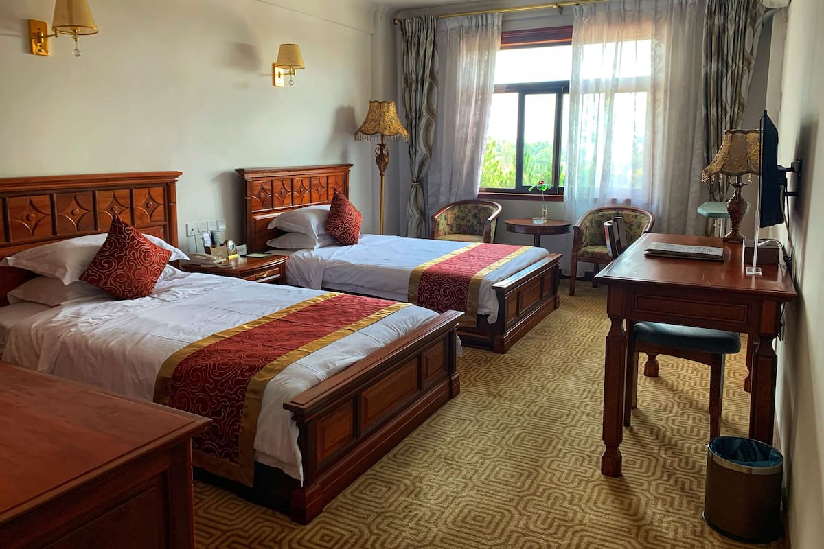 A hotel room with two beds, a desk, a chair, and a window with curtains.