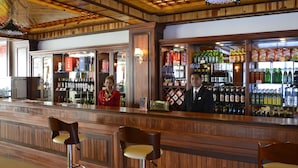 Een bar met houten lambrisering, een toonbank met twee barkrukken en gevulde flessenkasten.