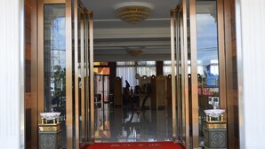 Een hotelingang met een rode loper, glazen deuren en twee sierlijke voetstukken aan de zijkant.