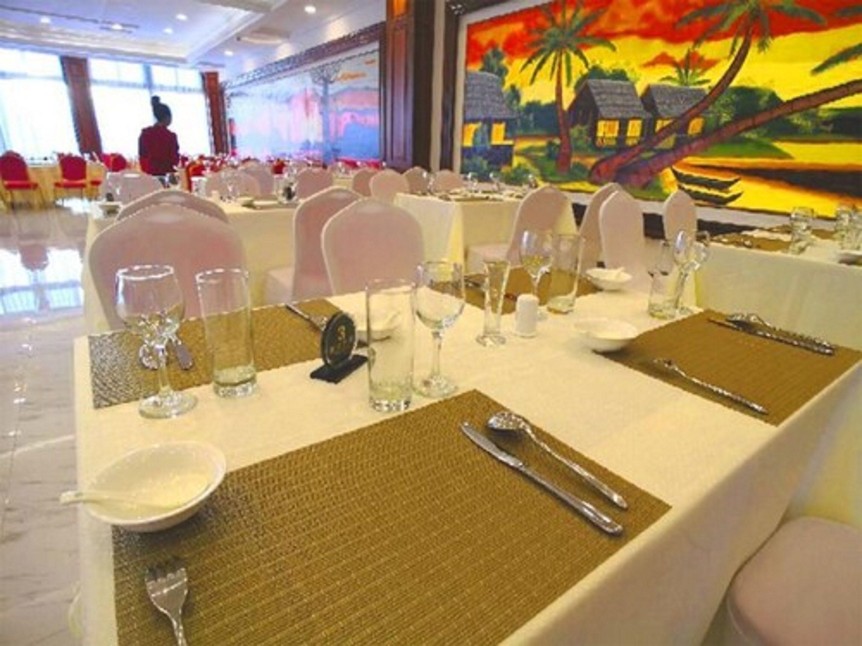 A banquet hall with round tables set for a formal event, featuring white tablecloths, clear glassware, and silverware.
