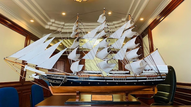 Een modelboot in een kamer met een kroonluchter en houten wandpanelen.