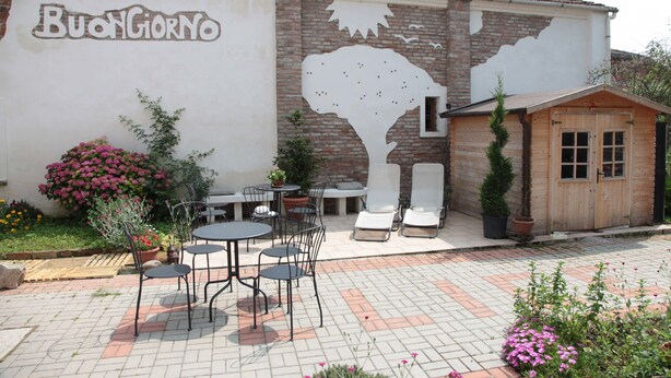 A courtyard with outdoor seating, a wooden structure, and a wall with a mural. - B&B Ciliegio Felice (Argenta)