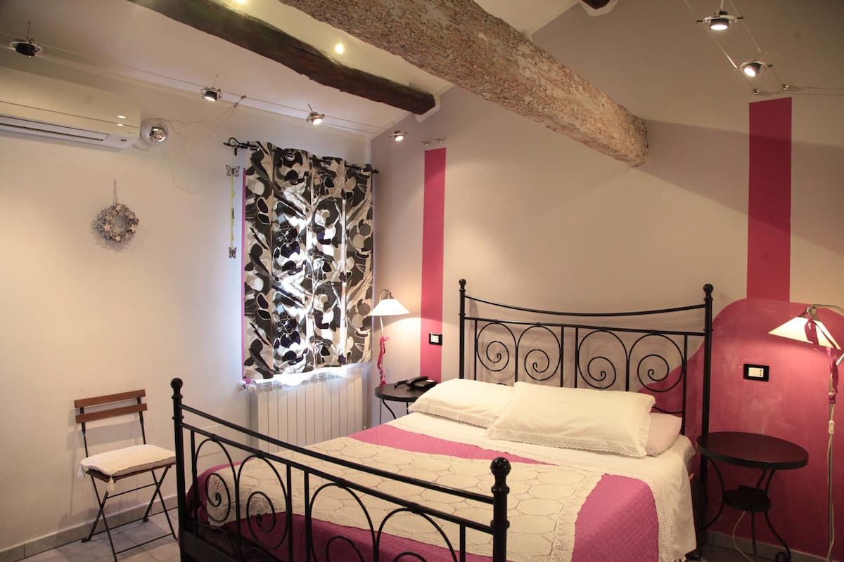 A bedroom with a bed, a chair, a table, and a window with curtains.