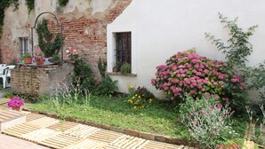 A garden with a brick wall, potted plants, and a wooden deck. - B&B Ciliegio Felice (Argenta)