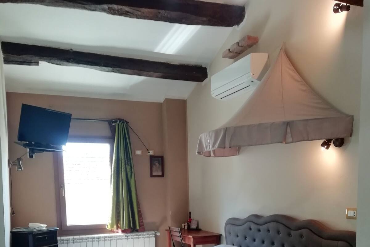 A bedroom with a bed, a desk, a chair, an air conditioning unit, and a television.