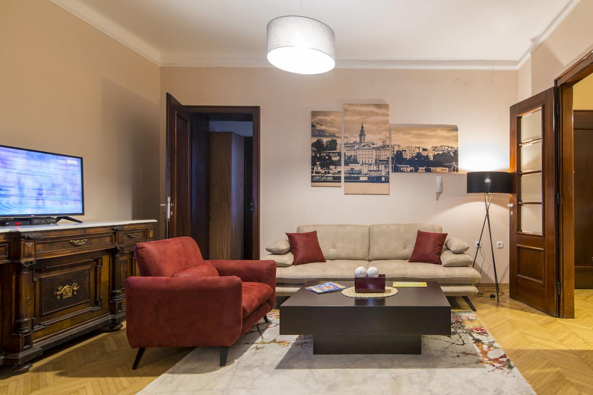 A living room with a sofa, red armchair, coffee table, TV, and artwork on the wall.