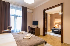 A hotel room with a bed, desk, laptop, and a view of another room.