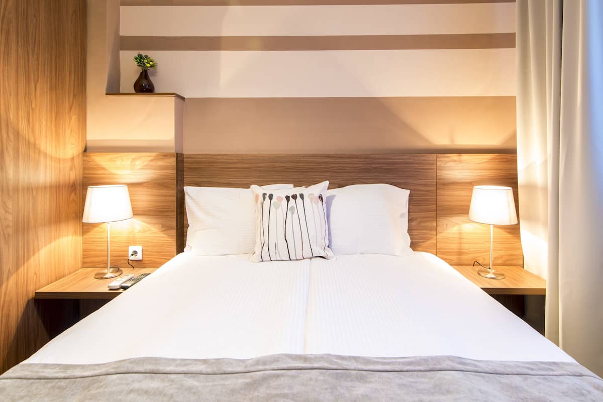 A neatly made bed with a wooden headboard, two bedside lamps, and a small plant on the nightstand.