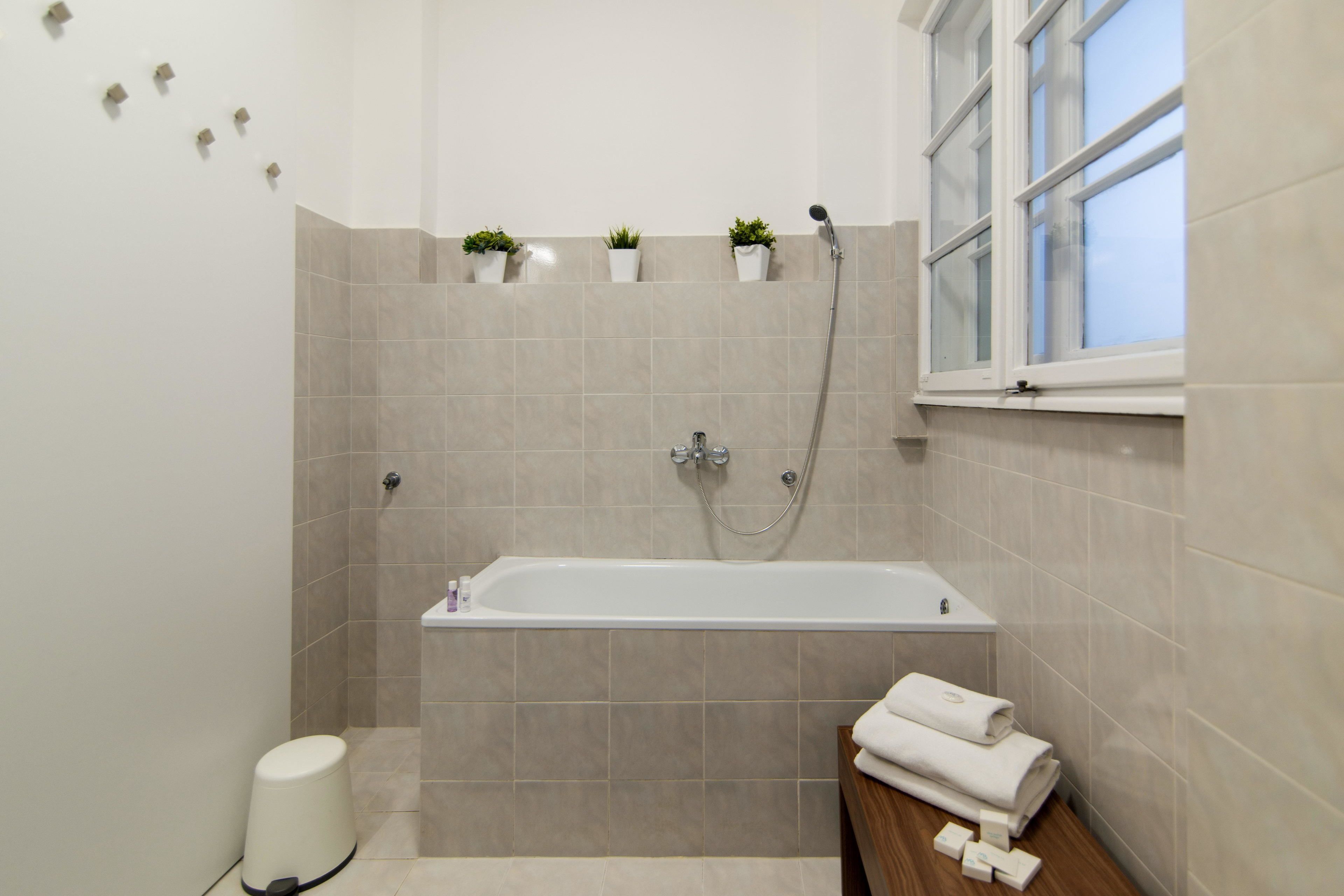 A modern bathroom with a bathtub, a window, and potted plants on the wall.