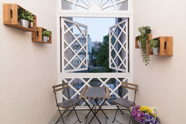 A balcony with two wooden chairs, a small table, and potted plants on wooden shelves.