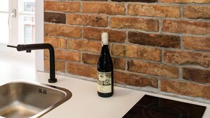 A kitchen with a brick wall, a neon sign spelling "Sydney," a stainless steel sink, and a bottle of wine. - Bliss Apartments Sydney (Poznan)