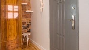 A hallway with a wooden floor, a brick wall, a grey door, and a small white stool. - Bliss Apartments Sydney (Poznan)