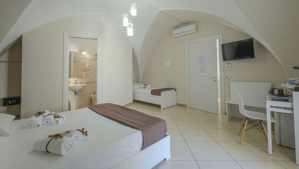 Une chambre d’hôtel moderne dotée d’un grand lit, d’un bureau, d’une chaise, d’une télévision et d’un plafond en arc de cercle.