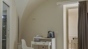 Une petite pièce bien éclairée, avec un bureau blanc, une chaise, une machine à café et un ordinateur portable.
