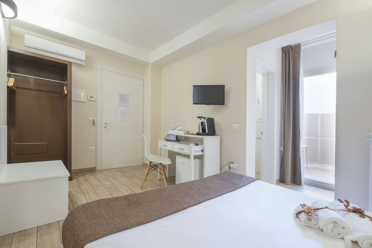 Habitación de hotel con cama, escritorio, silla, televisor y ventana con cortinas.