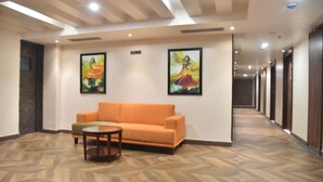 Un vestíbulo de hotel con piso de madera en patrón espiga, un sofá naranja, una mesita redonda y dos cuadros enmarcados en la pared.