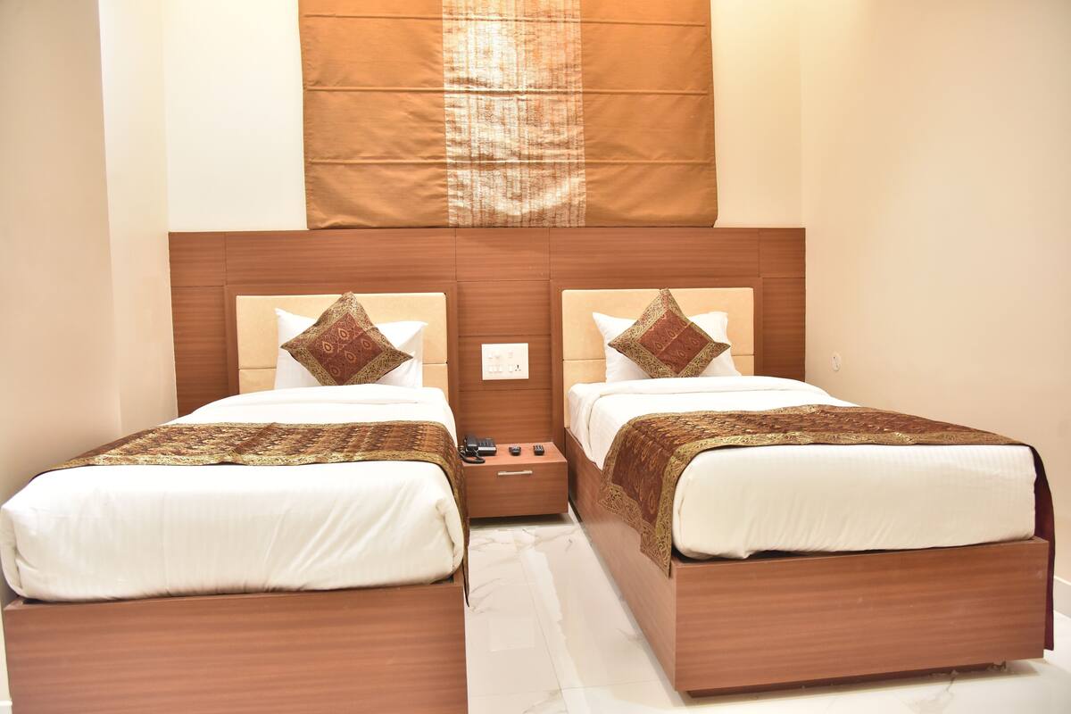 A hotel room with two beds, a wooden headboard, and a nightstand with a phone and remote control.