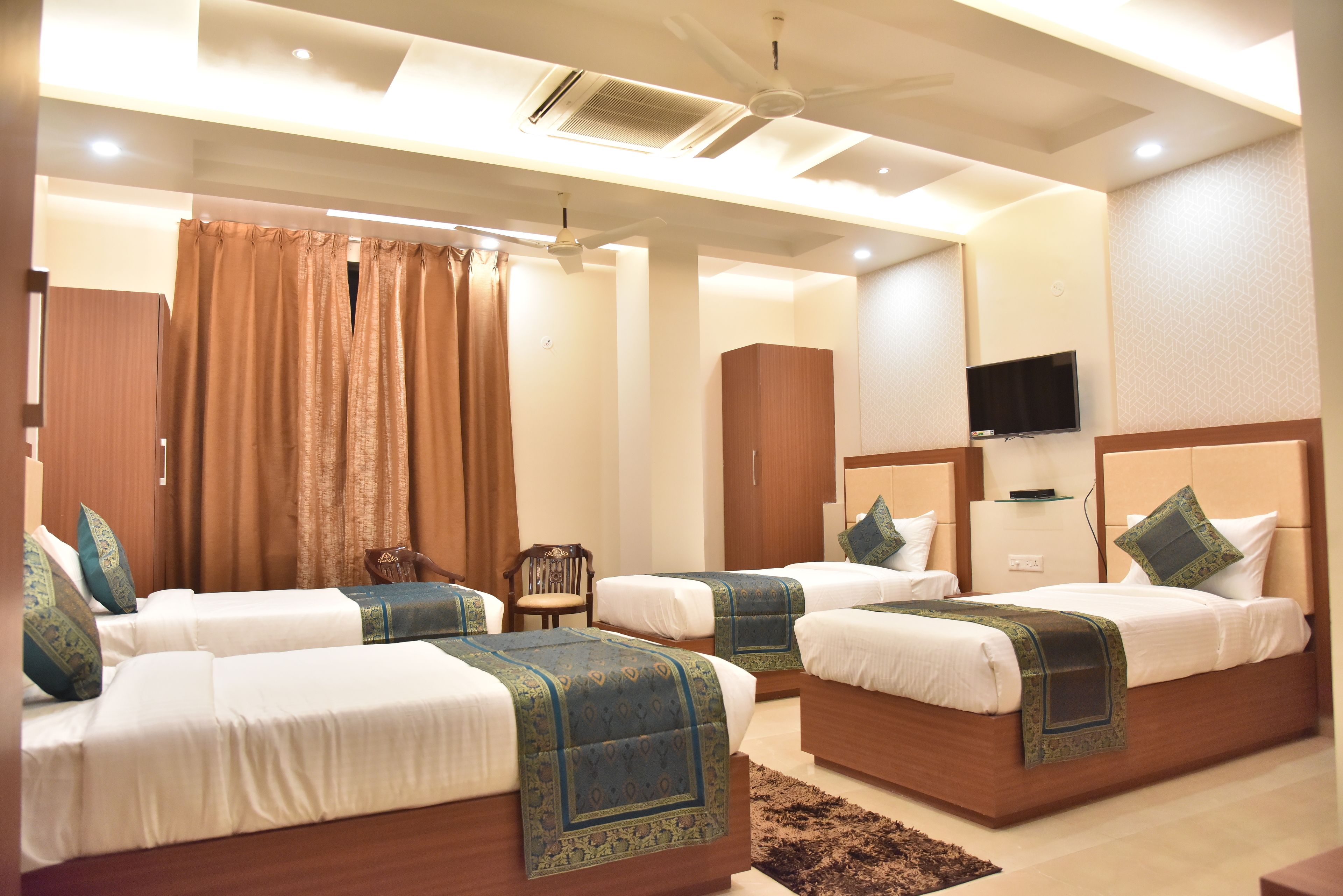 A hotel room with three beds, a television, and a ceiling fan.