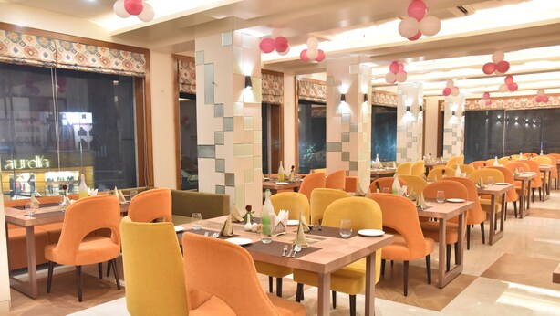 Un restaurante con sillas anaranjadas y amarillas, mesas con mantelería y globos rosados y blancos.