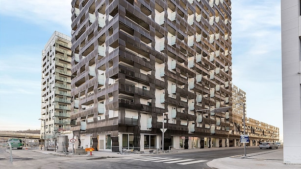 Um edifício moderno alto com fachada geométrica marcante, várias varandas e céu claro.