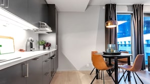 Uma cozinha moderna com armários escuros, bancada branca e um espaço de refeições com mesa e cadeiras.