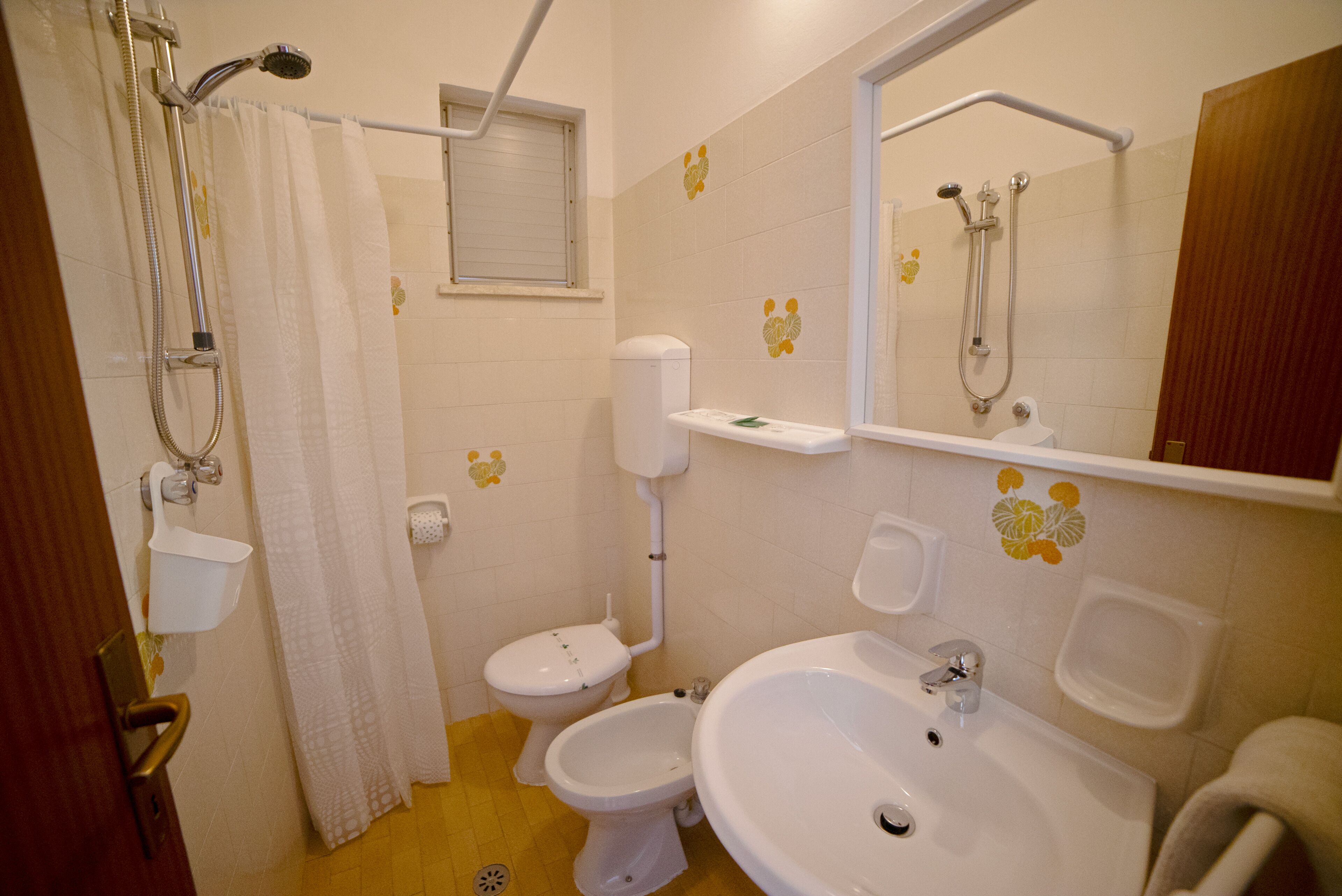 Ein Badezimmer mit Dusche, Toilette, Bidet, Waschbecken und Spiegel.