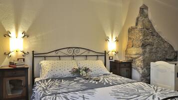 Una cama con colcha estampada, dos mesitas de noche con lámparas, una mesita auxiliar y un revestimiento de pared de piedra.