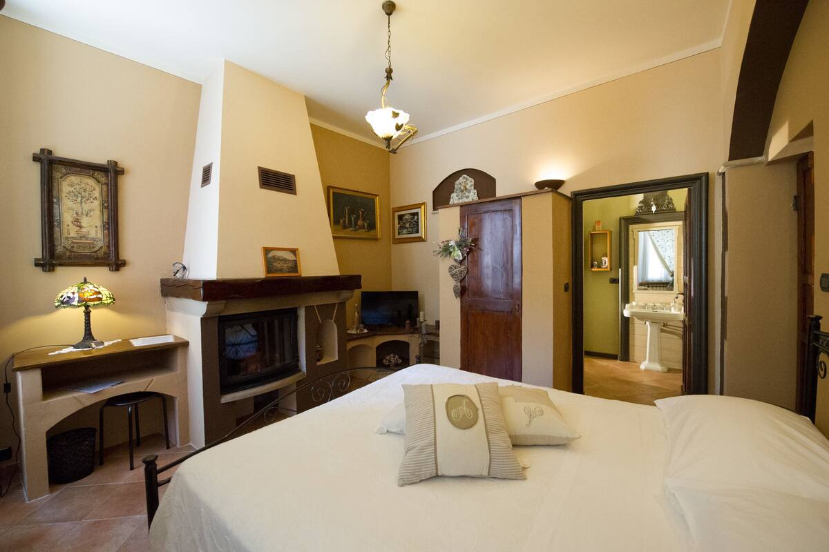 Un dormitorio con cama, escritorio, chimenea y espejo.