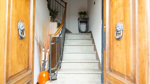 Un escalier dont les marches sont recouvertes d’un motif à carreaux, menant à un palier où se trouvent un pot de fleurs et une petite table.