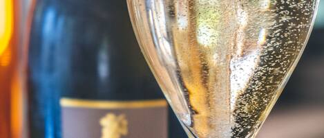 A glass of champagne with bubbles, a bottle of wine in the background, and a label with text.
