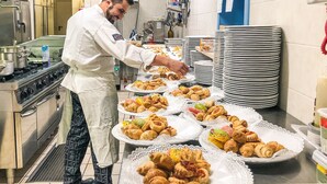 A kitchen with a chef preparing food, various cooking equipment, and a display of pastries on plates.
