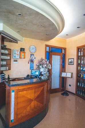 Zona de recepción con un mostrador de madera, un reloj, un certificado enmarcado y una exhibición de bebidas embotelladas.